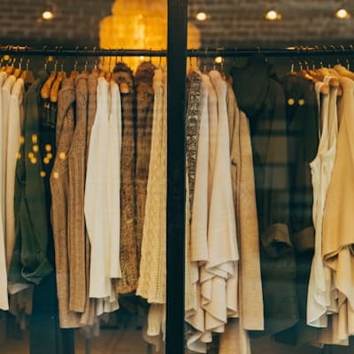 A rail of knitwear in neutral tones seen through a shop window