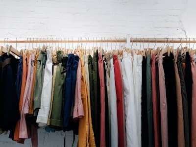 Trousers in assorted colours hanging on a rail against a white wall